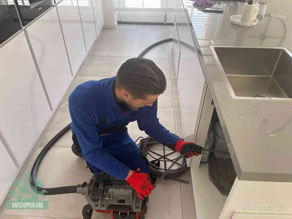 Een monteur ontstopt de keukenafvoer onder de spoelbak met een elektrische veermachine in Urk
