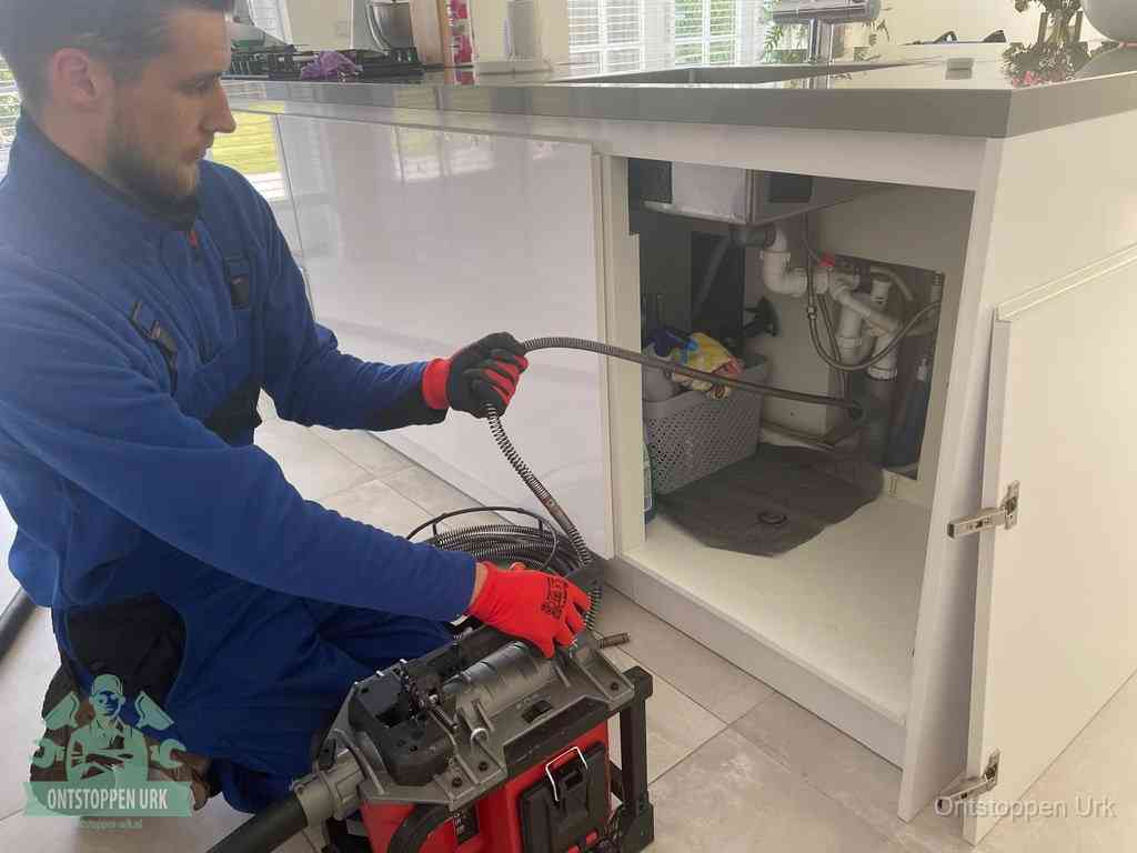 Monteur voert een ontstoppingsveer in de afvoer onder de keuken in Urk