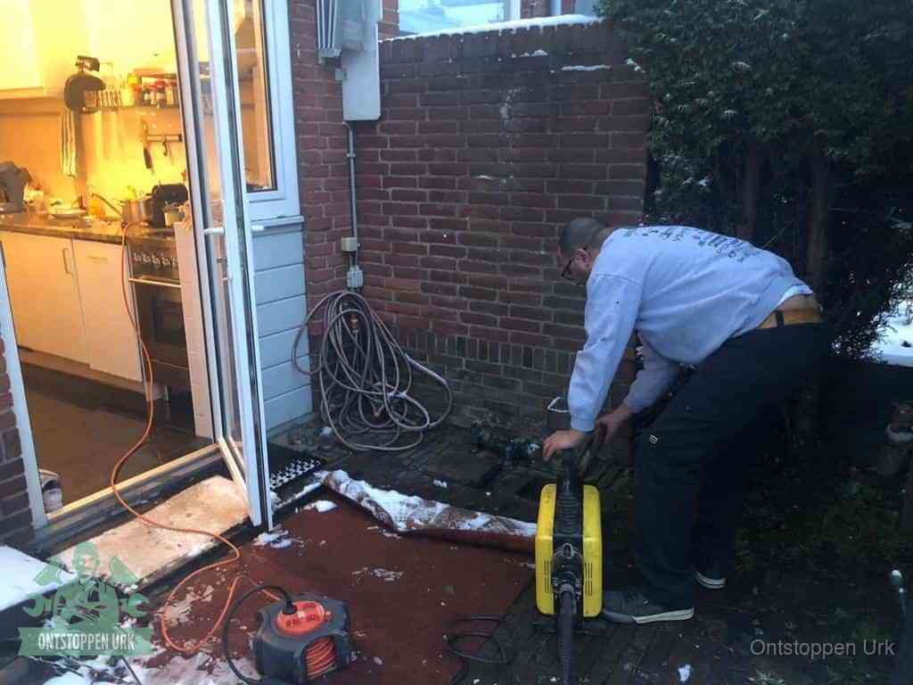 Een monteur werkt buiten bij een open riool-/grondput met een elektrische ontstoppingsmachine om een verborgen afvoerprobleem op te sporen in Urk