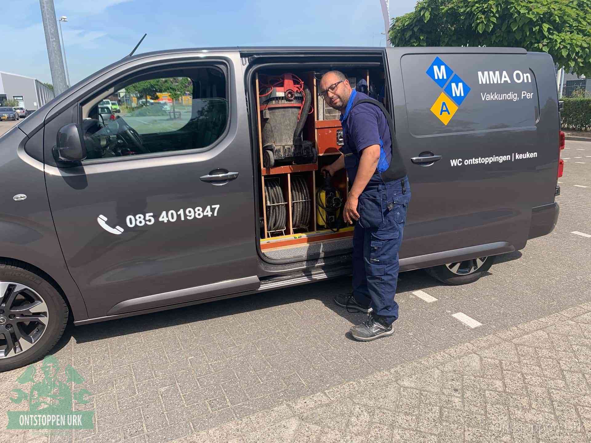 Een monteur bij de open schuifdeur van zijn bedrijfsbus op een parkeerplaats, klaar om de oorzaak van terugkerende afvoerverstoppingen aan te pakken in Urk