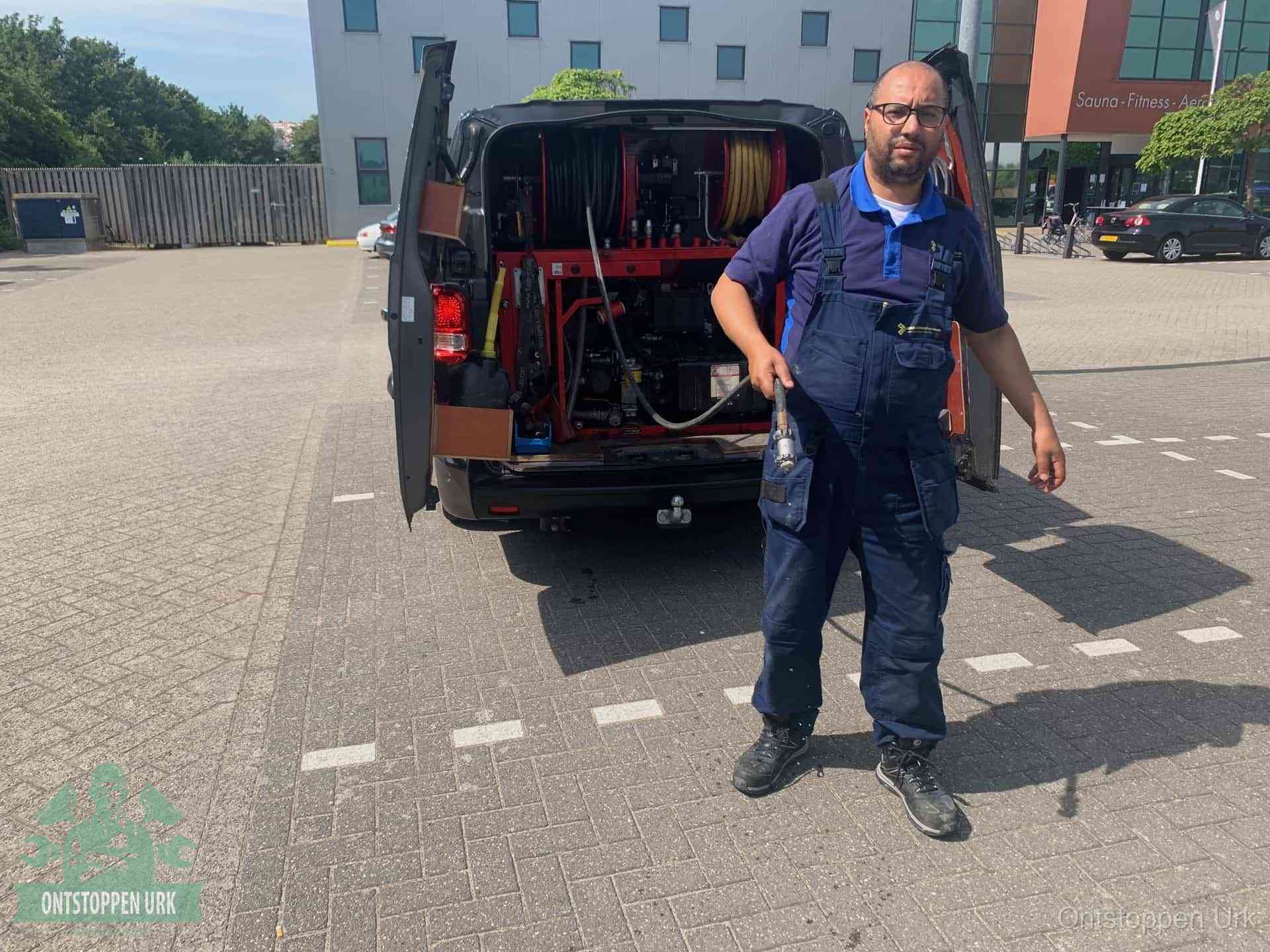 Een monteur bij zijn bestelbus met een hogedruk- en rioolreinigingsunit, klaar om de oorzaak van terugkerende wc-verstoppingen aan te pakken in Urk