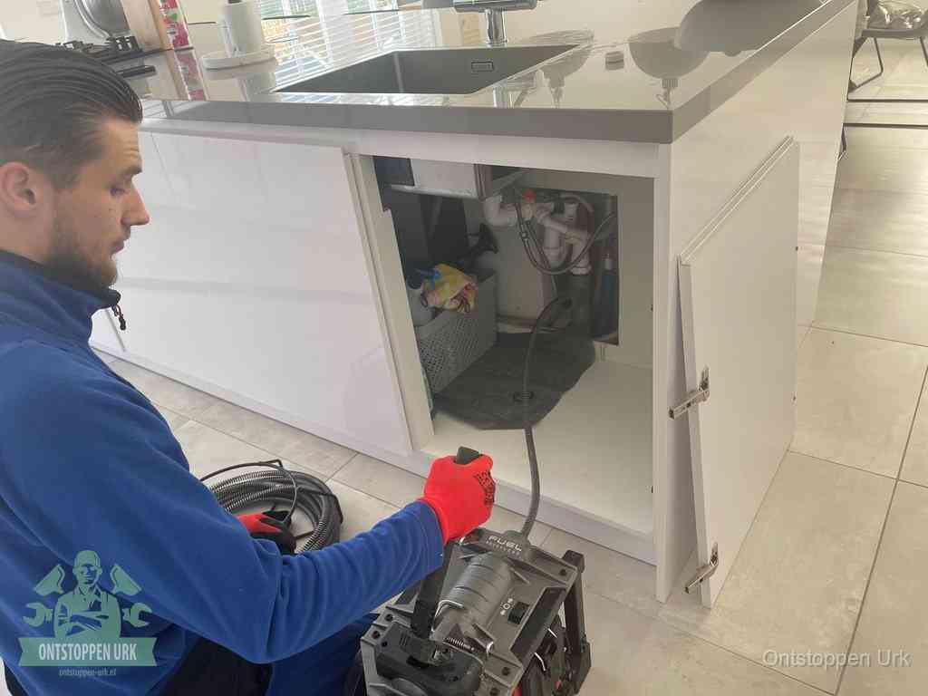 Monteur ontstopt met een veermachine een verstopte afvoer onder de gootsteen in Urk
