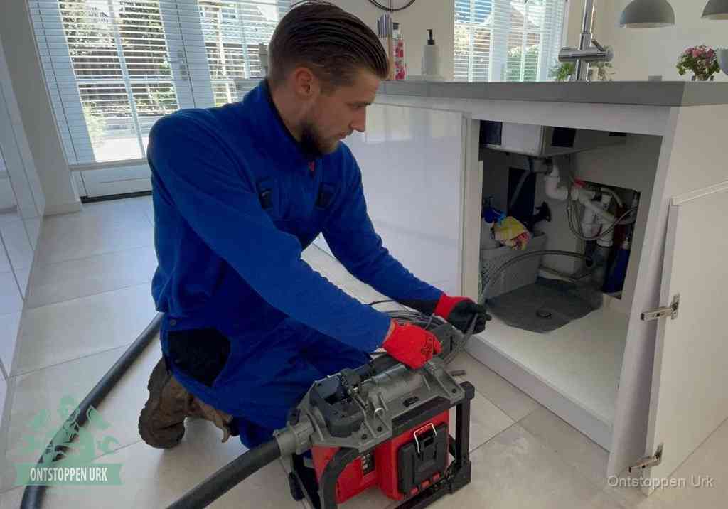Een monteur voert een professionele elektrische ontstoppingsmachine in de afvoer onder de spoelbak tijdens het gootsteen ontstoppen in Urk